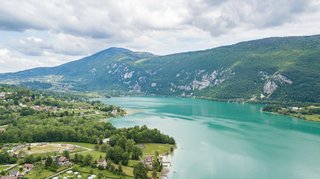 Panoramic view across Lac de Montbel with calm blue water, forested shores, and distant Pyrenees mountains