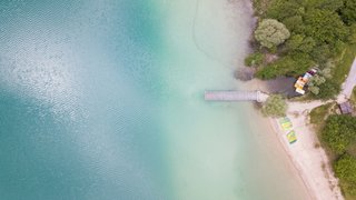 Des gens qui nagent et se détendent au bord du Lac de Montbel, avec une eau claire et un environnement montagnard pittoresque en Ariège Des gens qui nagent et se détendent au bord du Lac de Montbel, avec une eau claire et un environnement montagnard pittoresque en Ariège